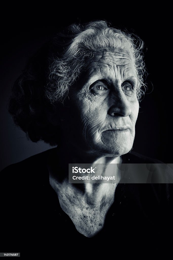 Older woman side portrait in dark setting Serene portrait of an old woman with white hair Black Background Stock Photo