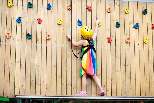 Child in forest adventure park. Kids climb on high rope trail. Agility and climbing outdoor amusement center for children. Little girl playing outdoors. School yard playground with rope way.
