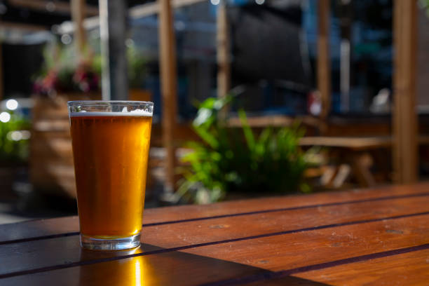 IPA Beer Sunlit A full pint of IPA beer outside on a picnic table. india pale ale photos stock pictures, royalty-free photos & images