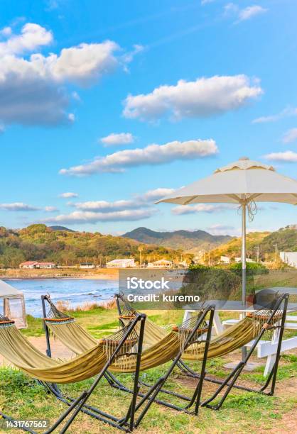 Hammocks And Wooden Outdoor Tables With Benches Overlooked By A Parasol Along The Coast Of Itoshima Beach Stock Photo - Download Image Now