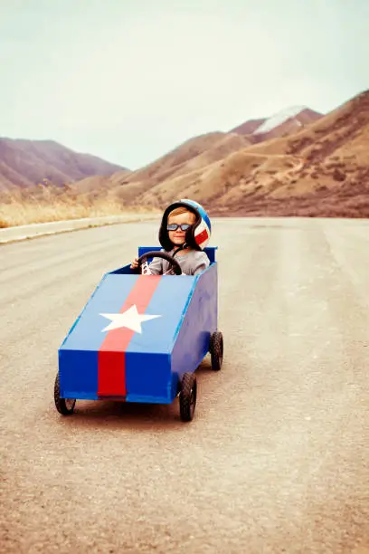 A young boy happily takes to the slope with his box car to test the limits of speed.