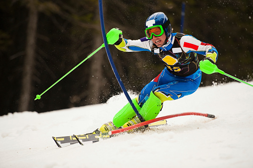 Front view of young male skier pushing the red and blue gate during the slalom ski race