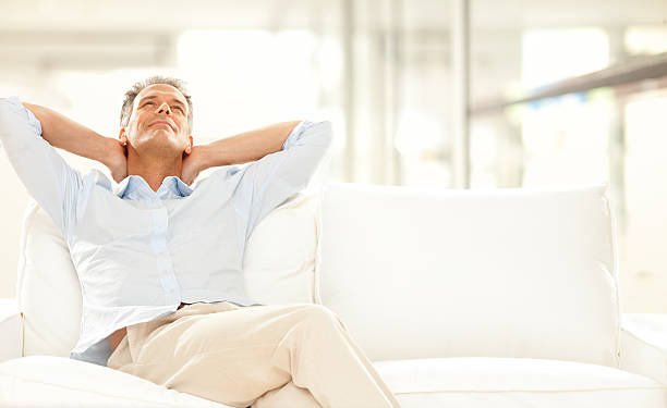Man with hands on his neck, relaxing on white sofa