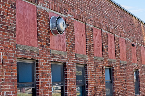 Windows on brick warehouse facade with ventilation fan. Building repurposed for other uses with original windows boarded up.