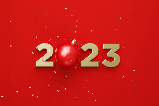Gold colored 2023 and red Christmas bauble sitting beneath falling confetti over red background. 2023 new year concept. Horizontal composition copy space. Directly above.