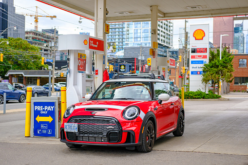 Toronto, Ontario, Canada- October 8, 2022. Chili red colour MINI COOPER on the gas station  in Toronto East side, Canada. This is a popular local meet of Cars & Coffee where various car enthusiasts get together. This is the third generation model F56 JCW, since BMW took over iconic brand of MINI. MINI featured in the photo is John Cooper Works model, the most powerful 2 door version. For the first time, this compact car features engine build and designed by BMW, and packs even more power and torque than previous models since 2002 to present. Original design clues and themes are still present on this brand new model. Mini has been around since 1959 and has been owned and issued by various car manufacturers.