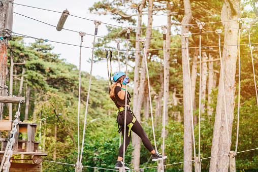 Girl athlete runs an obstacle course in climbing amusement park.Adventure park close-up. Summer fun and sports for adventurous people. Happy school girl enjoying activity in a climbing adventure park on a summer day.