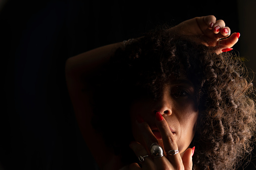 Close-up portrait of a woman with her hands on her face and head against black background. Joy concept. Salvador, Brazil.