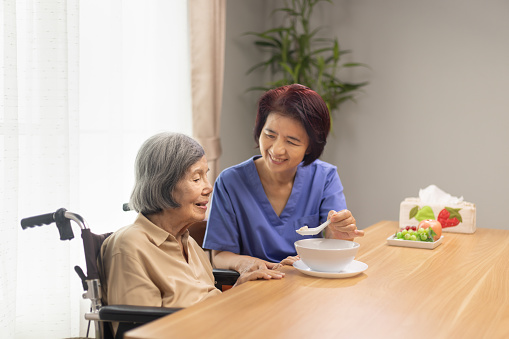 Caregiver feeding elderly asian woman with soup.
