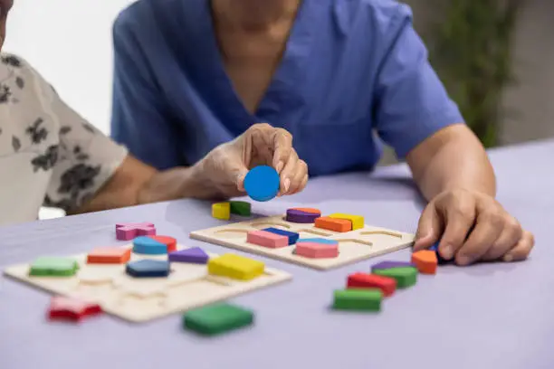 Caregiver and senior woman playing wooden shape puzzles game for dementia prevention