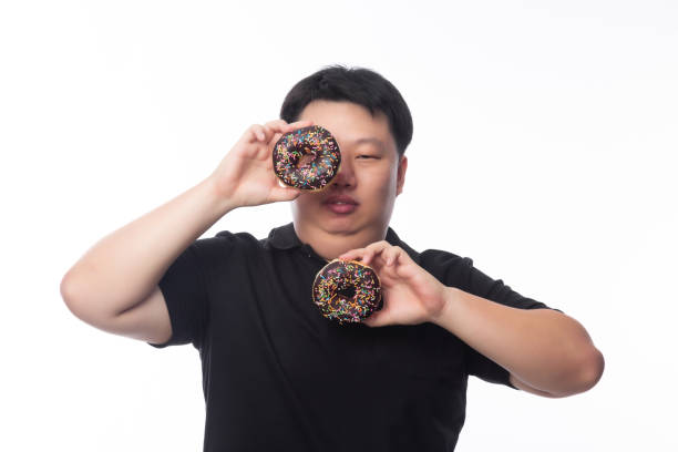 istock Young Funny Fat Asian man playing with chocolate donuts isolated on white background, Unhealthy concept 1431829884