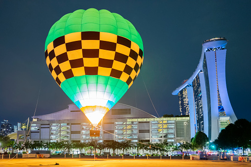Singapore, Singapore - October 8, 2022: A tethered hot air balloon operated by Ballons du Monde flies beside Marina Bay Sands and its convention centre at night.