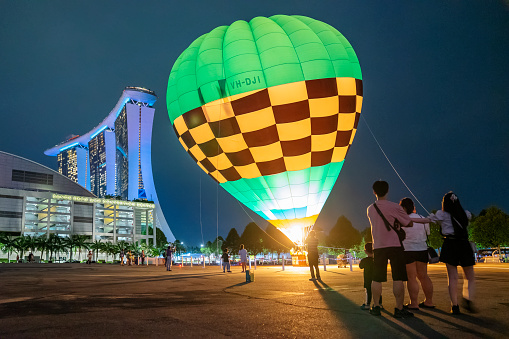 Singapore, Singapore - October 8, 2022: Spectators watch as a tethered hot air balloon operated by Ballons du Monde is set up at an open space beside Marina Bay Sands and its convention centre at night.