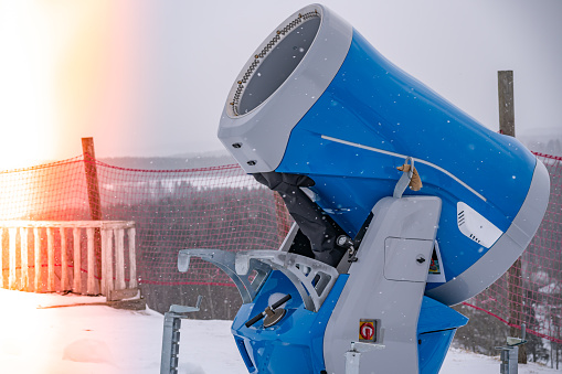 Snow cannon in winter mountains with flare. Snow-gun spraying artificial ice crystals. Machine making snow