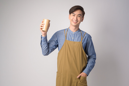 A Portrait of young asian man wearing apron holding paper cup over white background studio, Save earth concept.
