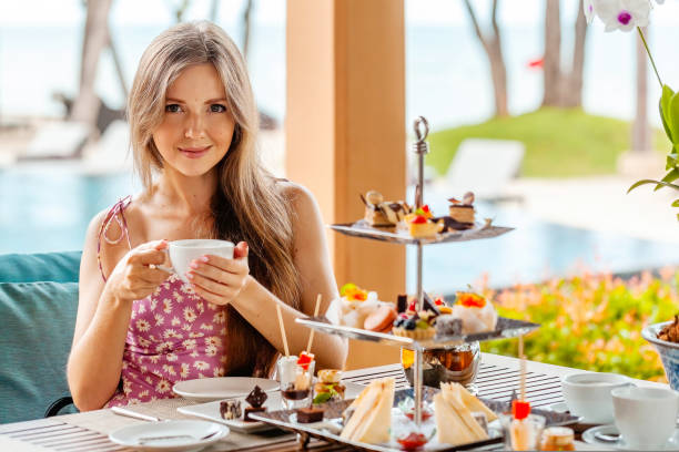 Woman sitting by table with high tea set in resort outdoors restaurant