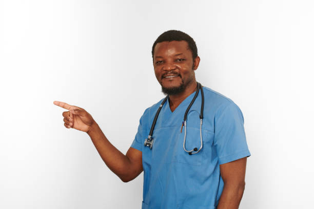 istock Smiling black surgeon doctor bearded man in blue coat with stethoscope points finger to left 1431855340