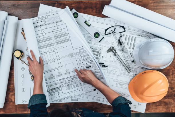 Top view Engineering working with drawings inspection on the office desk and Calculator, triangle ruler, safety glasses, compass, vernier caliper on Blueprint. Engineer, Architect, Industry and factory concept. vista superior ingeniería trabajando con inspección de dibujos en el escritorio de la oficina y calculadora, regla triangular, gafas de seguridad, brújula, pinza vernier en blueprint. ingeniero, arquitecto, industria y concepto de fábrica.