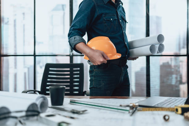 istock Engineering holding paper roll drawings in the office and Calculator, triangle ruler, safety glasses, compass, vernier caliper on Blueprint. Engineer, Architect, Industry and factory concept. 1431871594
