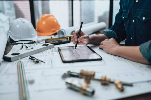 istock Engineering working with drawings inspection on tablet in the office and Calculator, triangle ruler, safety glasses, compass, vernier caliper on Blueprint. Engineer, Architect, Industry and factory concept. 1431872639