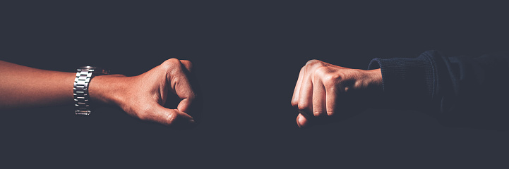 A shot crop of two fists smashing into each other to greet, challenge, fight, and duel.