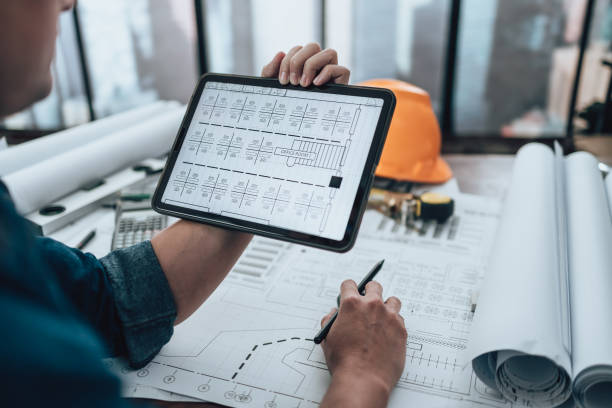 Engineering working with drawings inspection on tablet in the office and Calculator, triangle ruler, safety glasses, compass, vernier caliper on Blueprint. Engineer, Architect, Industry and factory concept. stock photo