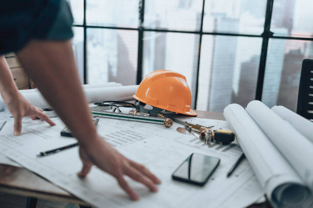 istock Engineer safety helmet with drawings inspection on the office desk and Calculator, triangle ruler, safety glasses, compass, vernier caliper on Blueprint. Engineer, Architect, Industry and factory concept. 1431875314