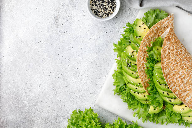 Green healthy sandwich with avocado, lettuce, sesame seeds. Flatbread, Vegetable Tortilla on grey background. Healthy snack. Copy space.