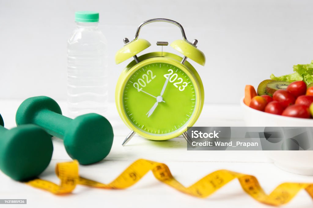 2022 and 2023 on alarm clock with workout planing for dieting. Sport exercise equipment workout and gym nutrition fresh salad for fitness. Merry Christmas and Happy new year concept New Year Resolution Stock Photo