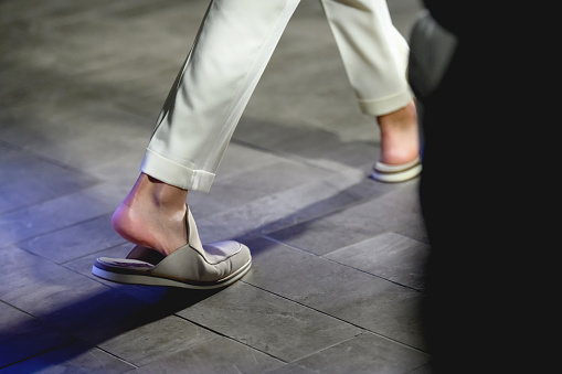 Low section of male fashion model walking on catwalk in sandals during fashion week