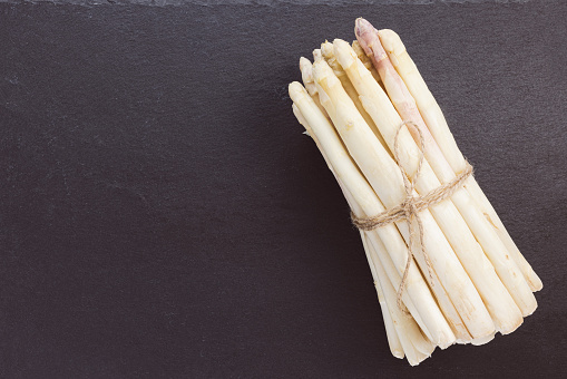 Bunch of fresh raw white asparagus spears on black background. Healthy greens, vegan food and ingredients for cooking concept. Closeup, copy space.
