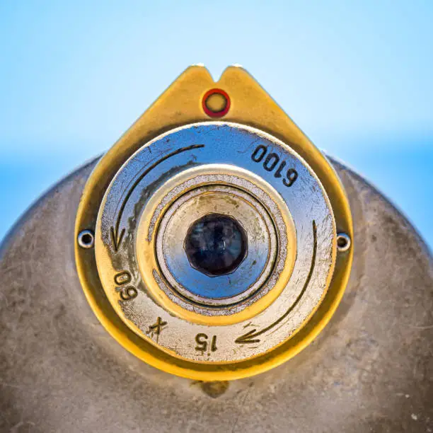 Photo of Rear view close-up color image of the brass colored focus eyepiece and aiming scope of an ordinary old steel telescope in the Algarve area of Portugal with blurred sea horizon in the background.