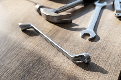 A portrait of  a hammer, a box end and an open end wrench lying on a wooden table. The tools are being used to perform a construction task or some kind of repair work.
