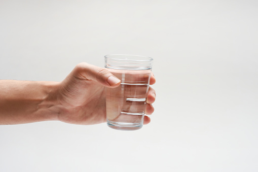 Drinking water, hand holding a glass of water with copy space