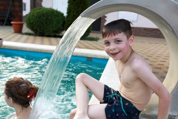 istock Boy sitting under stream of water in pool 1431901023