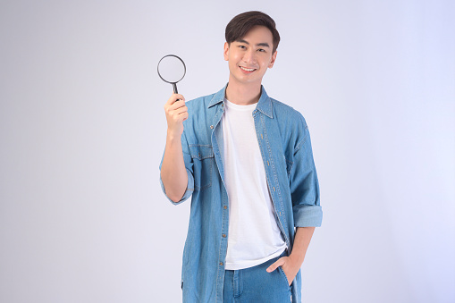 A Young asian man holding magnifying glass over white background, analysis and finance concept.