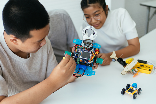 Focus select of a robot car with arm and teenagers trying to work on it
