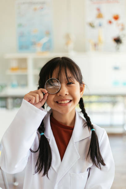 A young asian student plays around with a magnifying class in her classroom