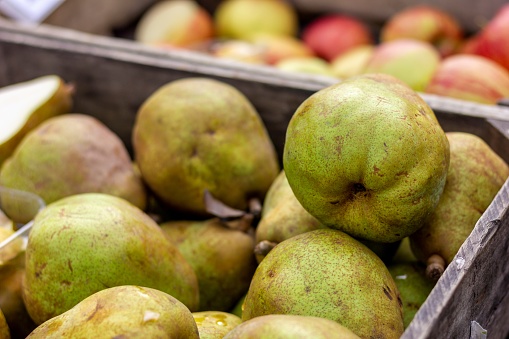 A portrait of a wooden crate full of pears at a local market. In the background there are blurred appels also in a wooden crate. The fruit is ready to get sold.