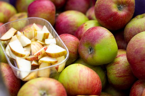 un ritratto ravvicinato di una cassa di legno piena di mele in un mercato locale. c'è un vassoio di plastica pieno di fette di mela per assaggiare la frutta per rendere il prodotto più attraente per i clienti. - half full apple green fruit foto e immagini stock