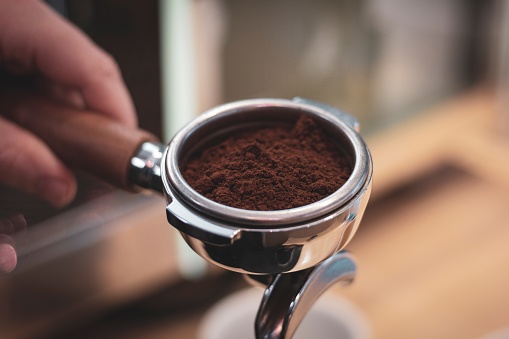 A close up portrait of a portafilter full of coffee grounds from freshly grinded coffee beans.