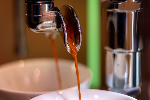 A close up portrait of fresh hot coffee running out of the portafilter of a coffee machine.