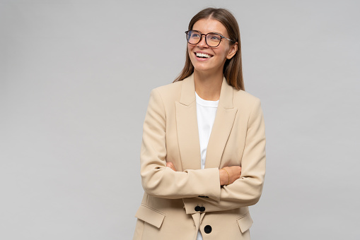 Portrait of happy cheerful student girl in glasses and stylish jacket standing on gray background with copy space on the right, looking up laughing