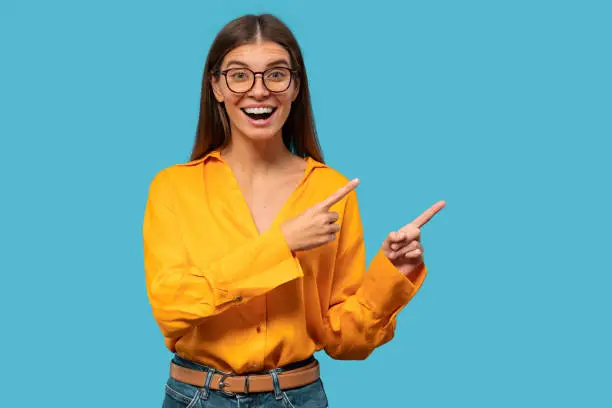 Photo of Excited young woman pointing with fingers to the side, showing unbelievable copy space for offer