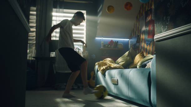 Boy pratices football before match in his room kicks the ball and performs trick stock photo