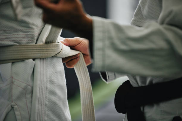 Karate learning, training and workout of a sport student and coach getting ready for a fight class. Defense expert hands tie a belt in a dojo, workout studio or wellness club about to work on fitness Karate learning, training and workout of a sport student and coach getting ready for a fight class. Defense expert hands tie a belt in a dojo, workout studio or wellness club about to work on fitness martial arts stock pictures, royalty-free photos & images