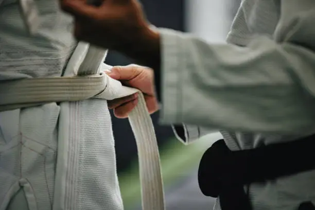 Photo of Karate learning, training and workout of a sport student and coach getting ready for a fight class. Defense expert hands tie a belt in a dojo, workout studio or wellness club about to work on fitness
