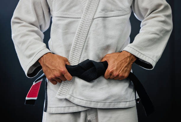 istock Professional karate master holding a black belt against a dark background in a dojo. Trainer, coach or leader prepared and motivated for training, fitness exercise and fight practice in a dojo 1431913684