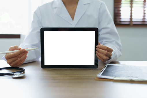 Asian female doctor holds computer tablet to customer, white screen can insert text or image.