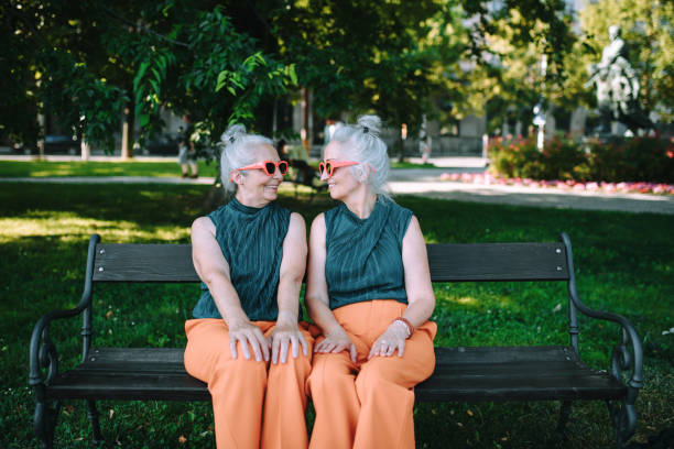 happy senior sister, twins sitting in city park and resting after shopping. - eeneiige tweeling stockfoto's en -beelden